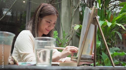 Happy young adult asian woman painting brush on canvas at workshop art lesson class outdoor cafe creativity hobby