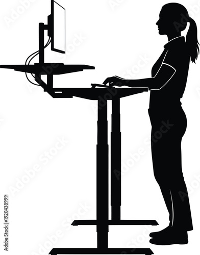 Silhouette of a woman working diligently on a computer while standing at an adjustable ergonomic standing desk in a modern office setting