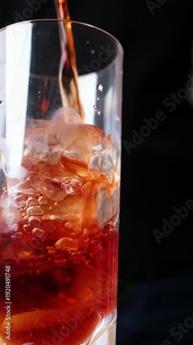 Slow motion pouring dark iced tea or cold beverage into glass with ice cubes.