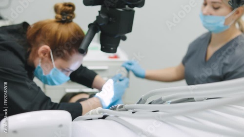 Two dental professionals assist a patient during a dental checkup, using tools and equipment for examination and care in the clinic.