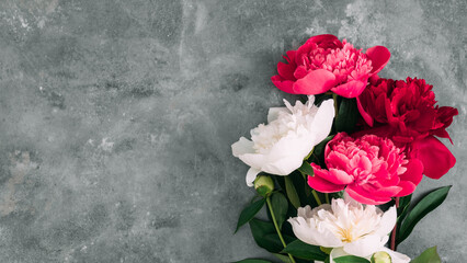 Top view of red and white peony flowers bouquet on grey stone background. Floral composition with copy space for text. Elegant flat lay for wedding, Mother's Day, or romantic greeting card.