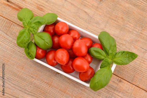 Cherry tomatoes, red and fresh, on a white plate, with basil. Vegetables on a wooden table.