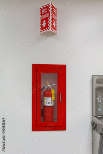 Fire extinguisher in a red wall-mounted cabinet with safety sign
