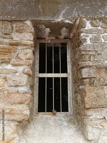 Old barred window in stone wall – concept of confinement and isolation