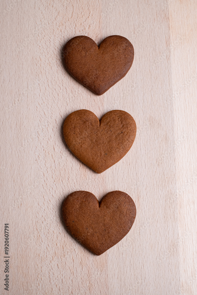 Obraz premium Three Heart-Shaped Gingerbread Cookies Arranged in a Row on a Light Wooden Surface. Top View
