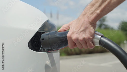 CLOSE UP: Young man charging luxury white Tesla electric car on beautiful day