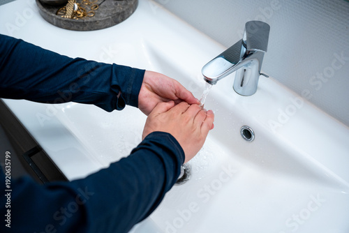 Close up of male hands washing with soap in clean white minimalistic porcelain sink. Daily hygiene routine: Person washing hands in a bright modern bathroom interior.