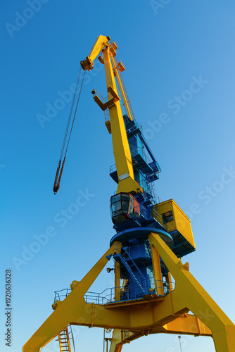 Yellow and blue industrial harbor crane with hanging chains, set against a clear blue sky