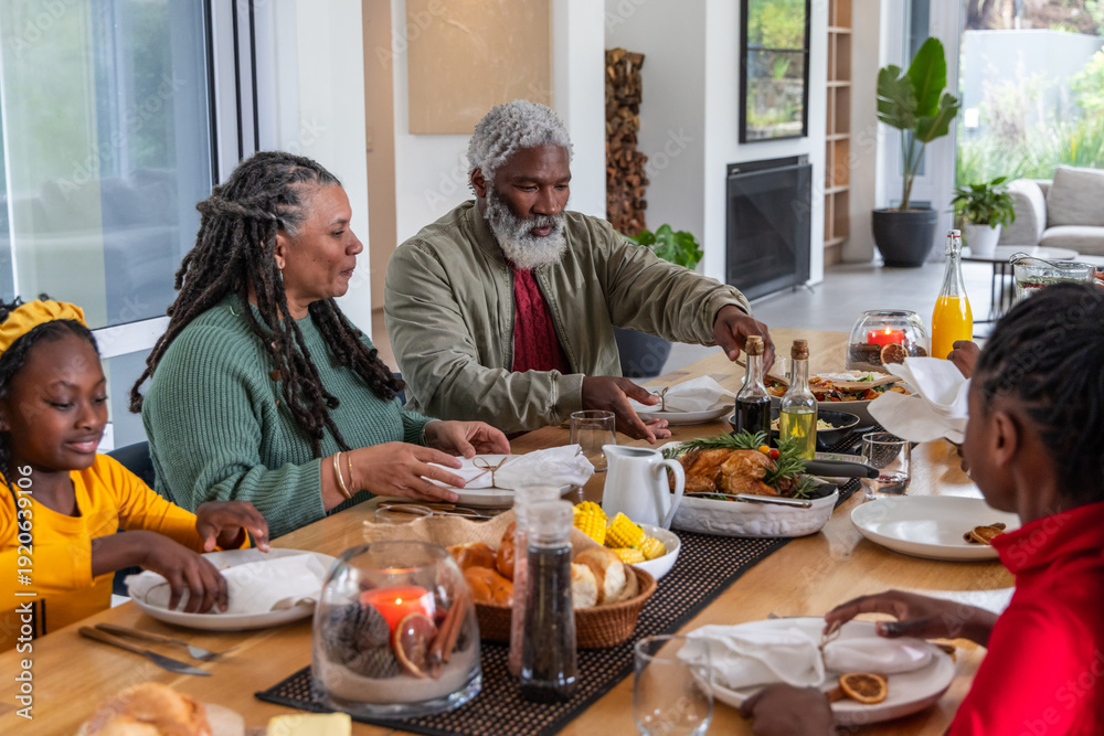 Fototapeta premium African American family passing dishes and serving roasted chicken at long wooden dining table