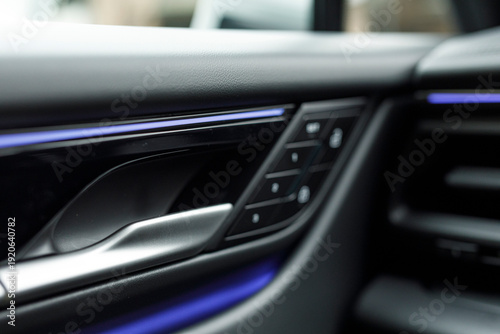 Close up of a modern car interior.  Door handle and control panel with soft lighting.  Stylish and clean automotive desi