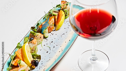 Luxury seafood appetizer paired with a glass of red wine, featuring seared fish and vibrant tuiles