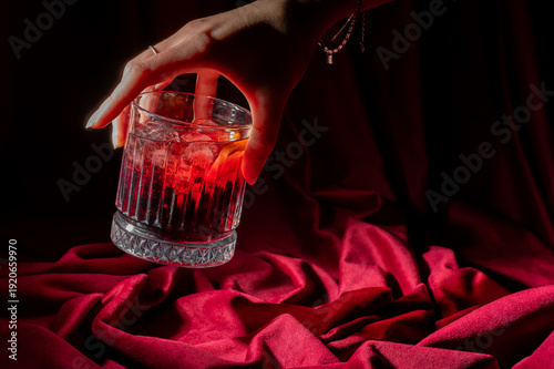 Fotografie Hand holding a classic Negroni cocktail in a fluted glass, set against a luxurio