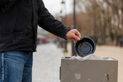 Un homme jette un emballage plastique dans une poubelle en ville