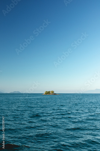 Small island surrounded by clear water under blue sky near coastal area during daytime hours