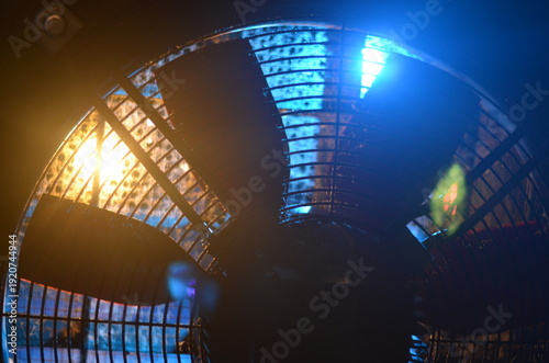 Close-up of electric fan with dramatic blue and orange lighting, glowing reflections and lens flare, abstract industrial technology background.