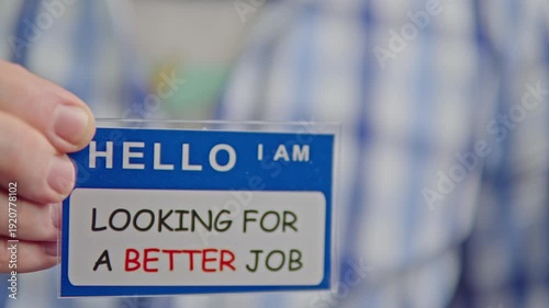 Man holding nametag reading looking for a better job, old wrinkled shirt,hopeful tone, informal