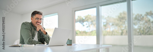 Принти на полотні Smiling wearing eyeglasses looking at computer sitting at table