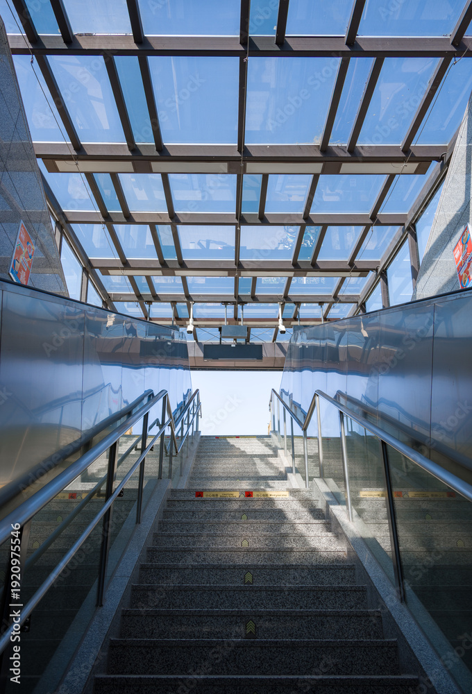 Obraz premium Ascending staircase in a metro station with glass roof and geometric metal structure under sunlight