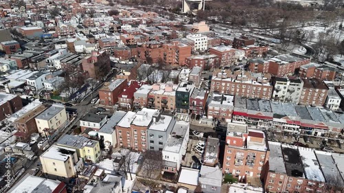 Aerial drone footage capturing a sprawling residential district with brick apartment buildings and houses, their rooftops lightly dusted with snow on a cold, sunny winter day in the city