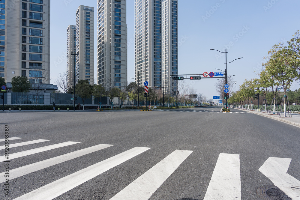 Fototapeta premium Empty urban street with tall modern buildings and clearly marked zebra crossing under clear blue sky