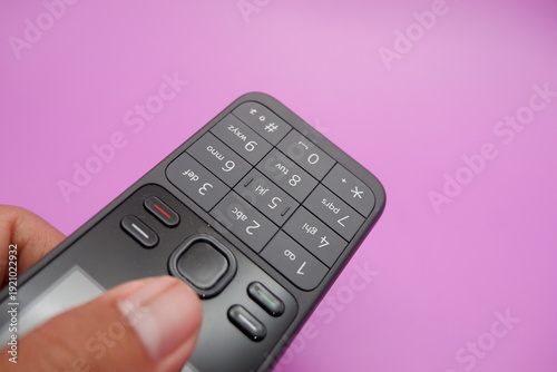 Hand Holding Classic Keypad Mobile Phone on Purple Background