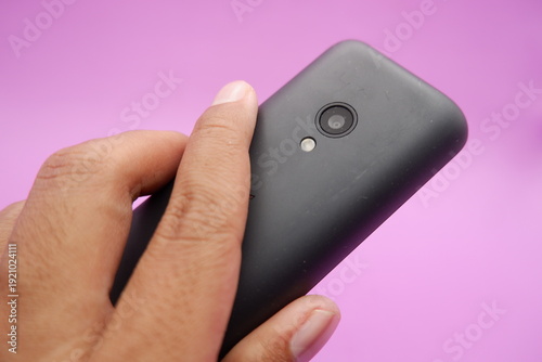 Hand Holding Classic Feature Phone with Rear Camera on Purple Background