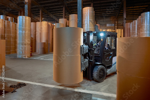 Forklift moving large paper rolls in a spacious warehouse at a paper mill during nighttime operations