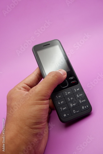 Hand Holding Classic Keypad Mobile Phone on Purple Background