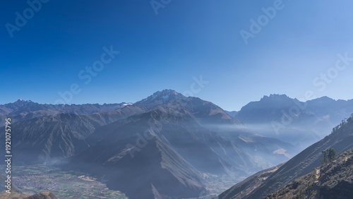 Highlands. A beautiful mountain range. Snow-capped peaks against a clear blue sky. There are rural houses and cultivated fields in the valley. Copy space. Peru.