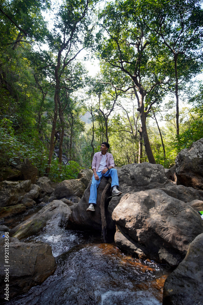 Obraz premium Young man relax on rock amidst forest stream, serene nature escape