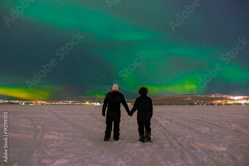 Couple sharing a romantic moment under the mesmerizing northern lights in Akaslompolo, Lapland