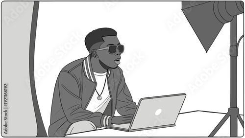 Young man in sunglasses working on laptop in a studio setting.