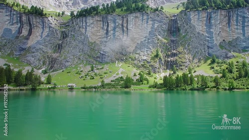 A breathtaking panoramic view of a pristine alpine lake nestled at the base of a towering rugged mountain cliff showcasing the serene beauty of untouched nature and majestic landscapes under a clear .