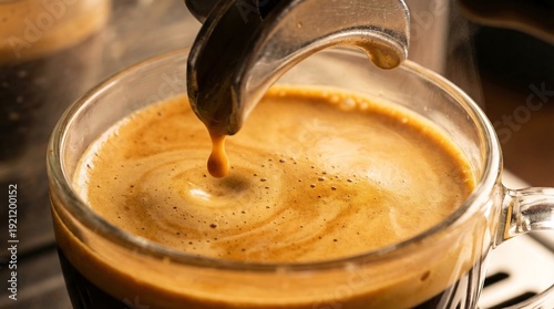 Freshly brewed rich espresso coffee pouring into a glass cup with thick golden crema