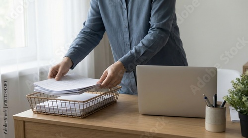 Professional organizing documents at work desk, hands placing paperwork into an inbox tray for efficient management and productivity