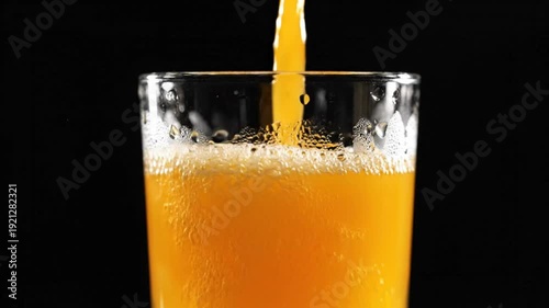 Close-up of fresh orange juice being poured into a clear glass against a black backdrop