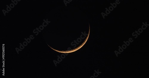 Timelapse of young crescent moon movement during moonset with passing clouds