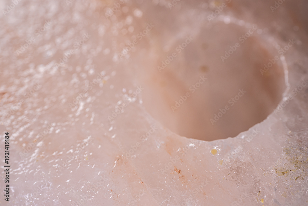 Fototapeta premium Close-up view of a translucent pink Himalayan salt block with a circular hole, showcasing the unique crystalline structure and texture of the mineral