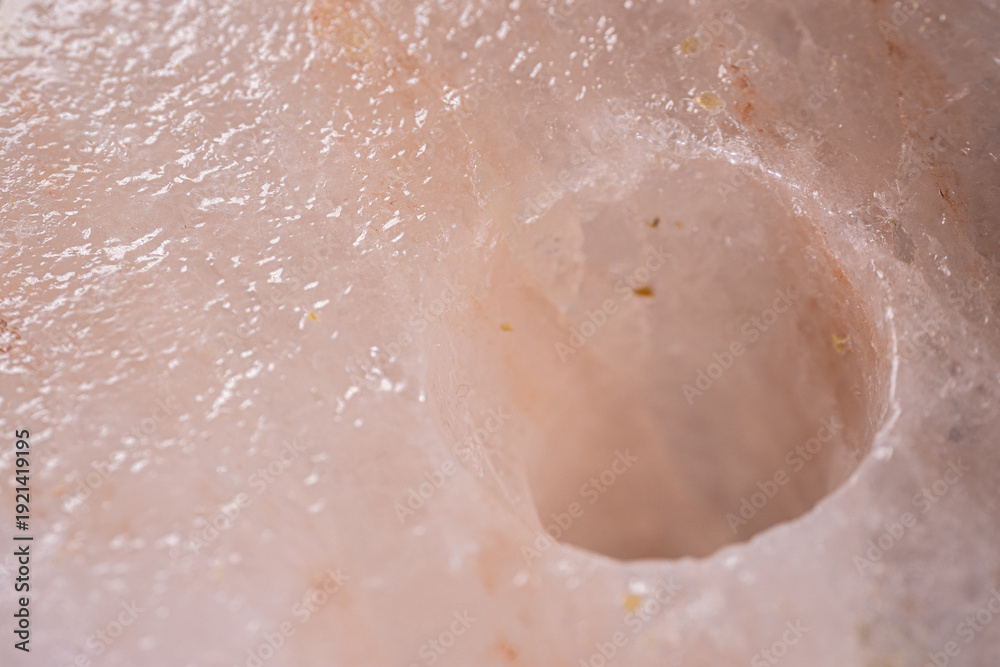 Fototapeta premium Close-up view of a pink Himalayan salt block with a circular indentation, showcasing the unique texture and mineral inclusions of the natural salt formation
