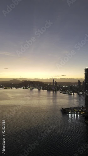 Cinematic aerial drone footage of the sunset over Cinta Costera in Panama City. The golden light of the sunset illuminates the coastal skyline, oceanfront boulevard, and modern buildings of the city, 