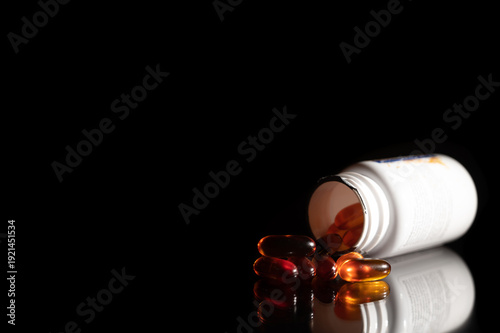 Transparent yellow Pills spilling out of pill bottle on black background with reflection from the surface.