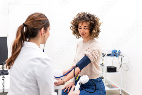 Photos Smiling female doctor measuring blood pressure of curly hair woman in medical clinic