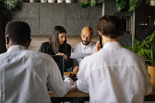 International team collaboration during a business meeting in a modern office, focusing on project details and teamwork around a wooden table in the afternoon
