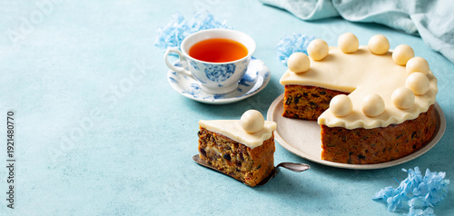 Simnel cake with marzipan balls served with a cup of tea. Traditional Easter treat. Blue background. Close up. Copy space.