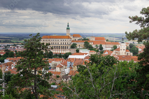 Beautiful landscape view of Mikulov Castle and town framed by green pine trees under a cloudy sky in the Palava wine region