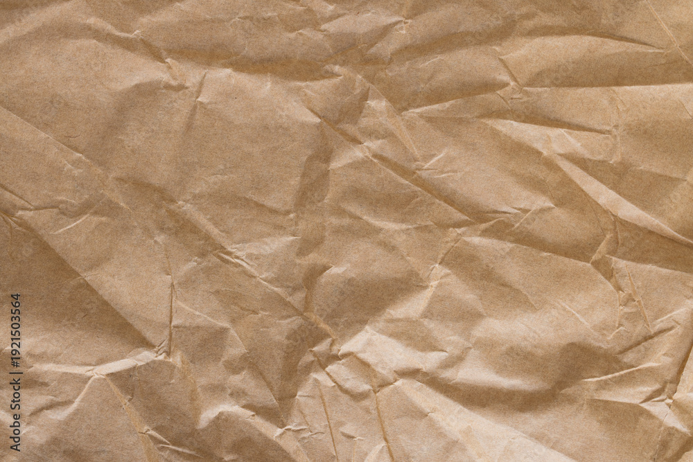 Obraz premium Crumpled Brown Kraft Paper Texture Background,Top view of creased and crumpled brown kraft paper texture. Abstract background of wrinkled recycled paper sheet with organic folds and shadows.