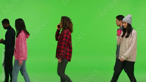 A diverse group of young adults walk across a green screen background, some looking at their phones, others talking.