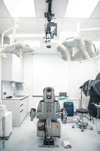Empty modern medical dental operating room featuring a specialized surgical chair, overhead surgical lights, and advanced medical equipment in a sterile