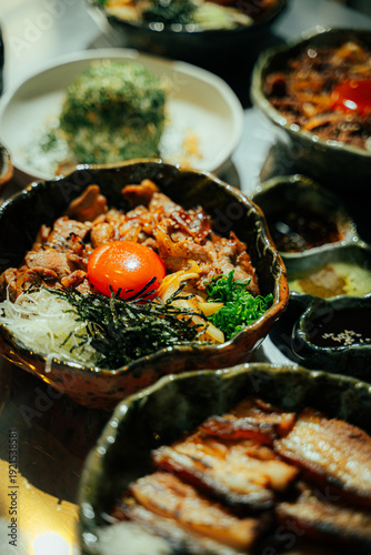 Close-up of a traditional Japanese beef rice bowl (donburi) topped with fresh raw egg yolk, shredded nori seaweed, green onions, and caramelized onions. Served in a rustic ceramic bowl with grilled po