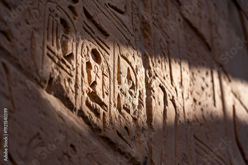 Close up of ancient Egyptian hieroglyphics and sacred symbols carved in sandstone with dramatic sunlight at Karnak Temple